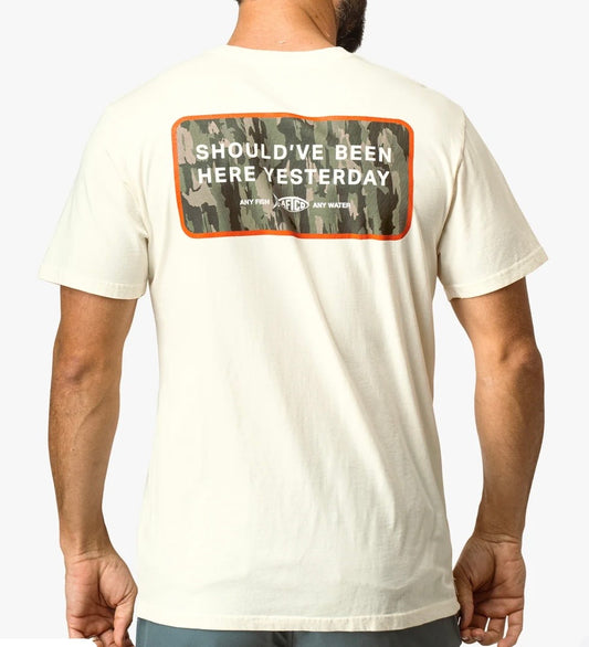 White t-shirt with text on the back worn by a person, against a plain background