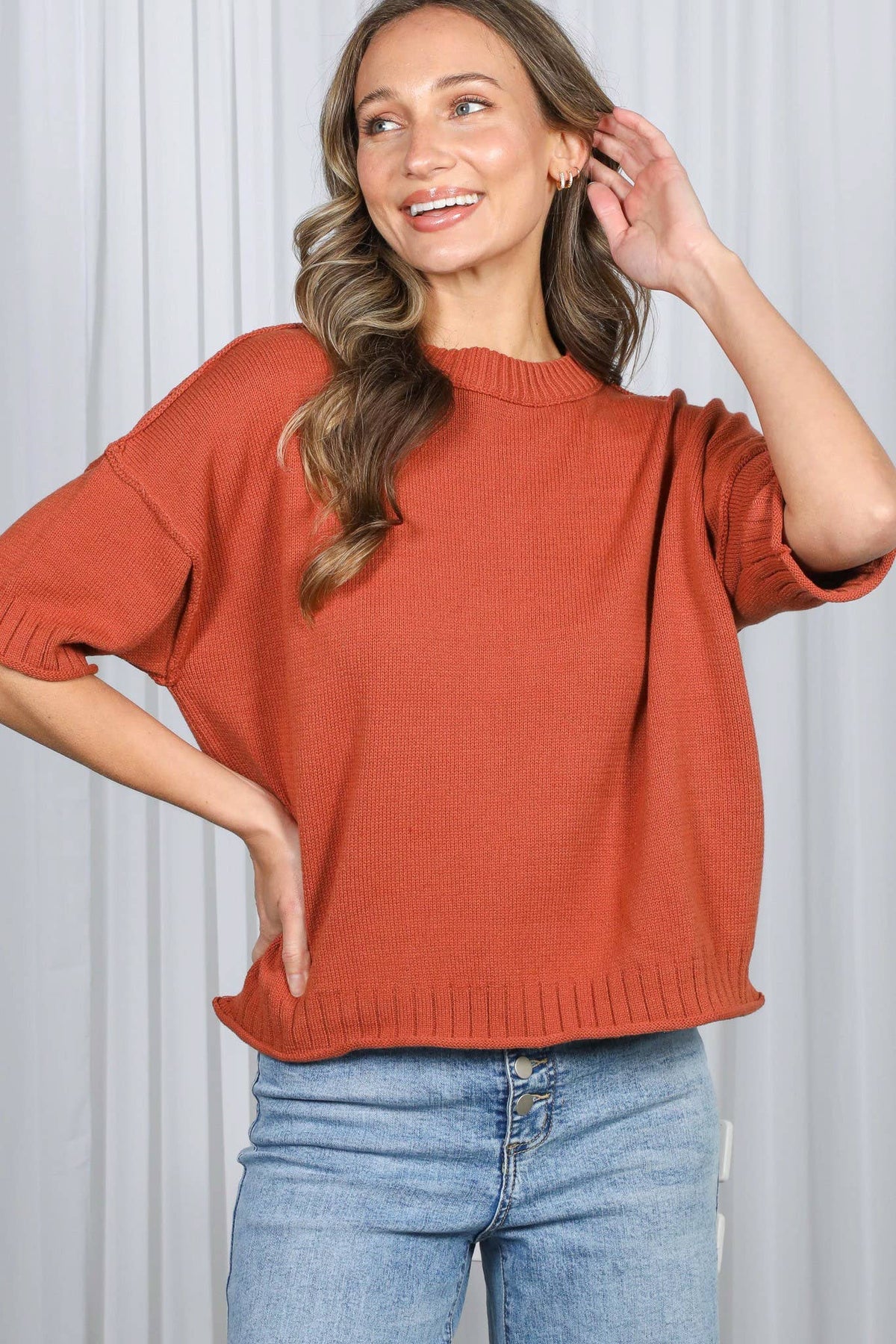 Woman wearing a rust-colored sweater and blue jeans against a white background