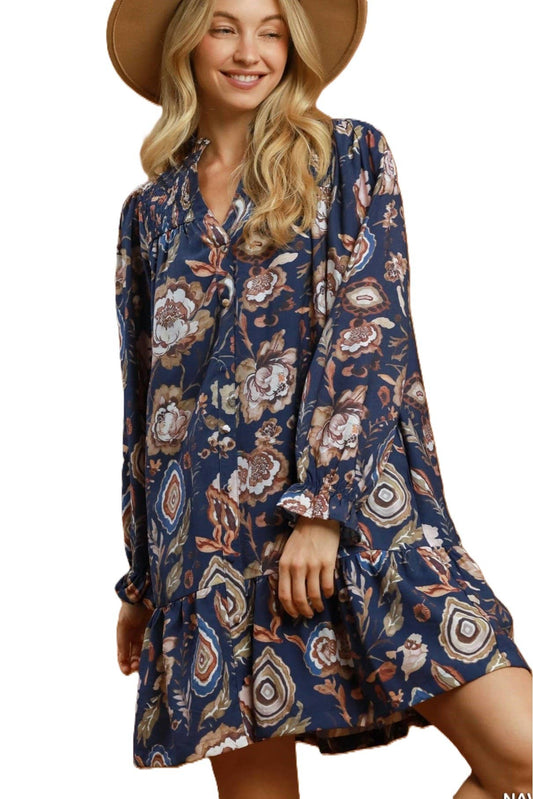 A woman wearing a navy blue long-sleeve mini dress with a beige, brown, and white floral pattern, paired with a wide-brimmed tan hat, set against a plain white background.